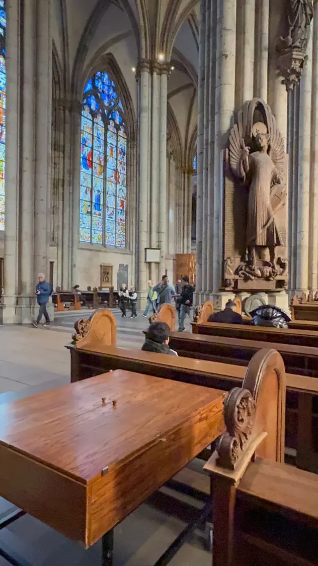 Stained glass windows in the aisle of Cologne Cathedral, with a carved winged figure on a pillar