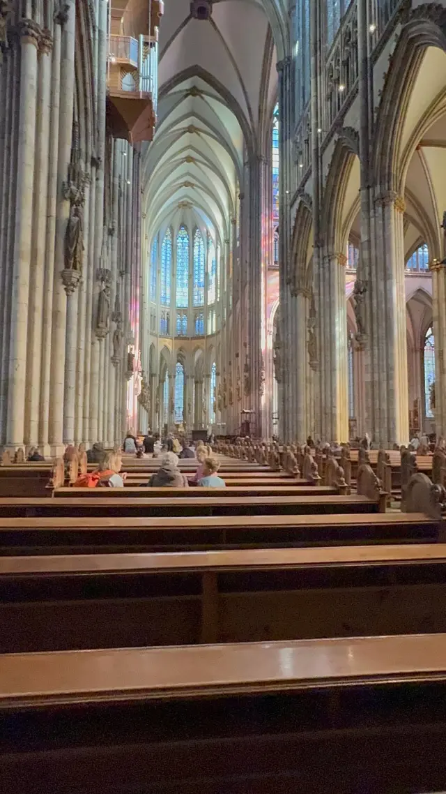 The nave of Cologne Cathedral seen from the pews, with coloured light from the windows on the pillars